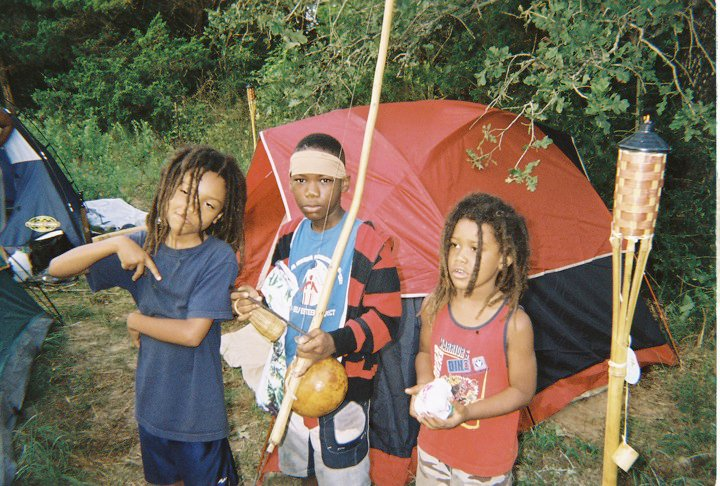 A kikosi of three boys at a red tent