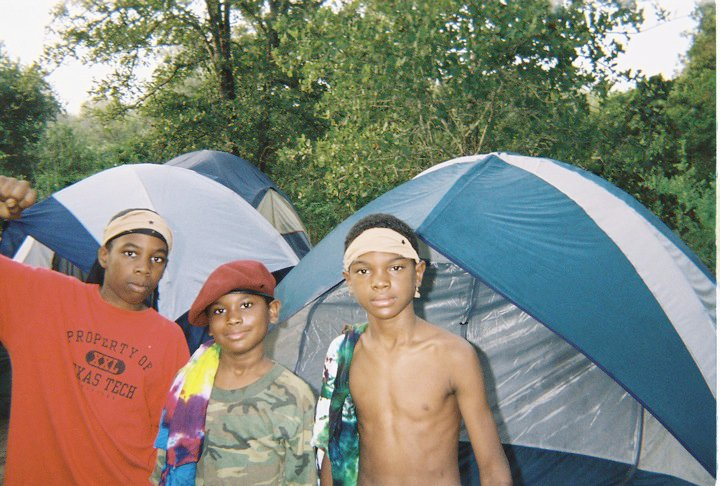 Three boys standing in front of camping tents